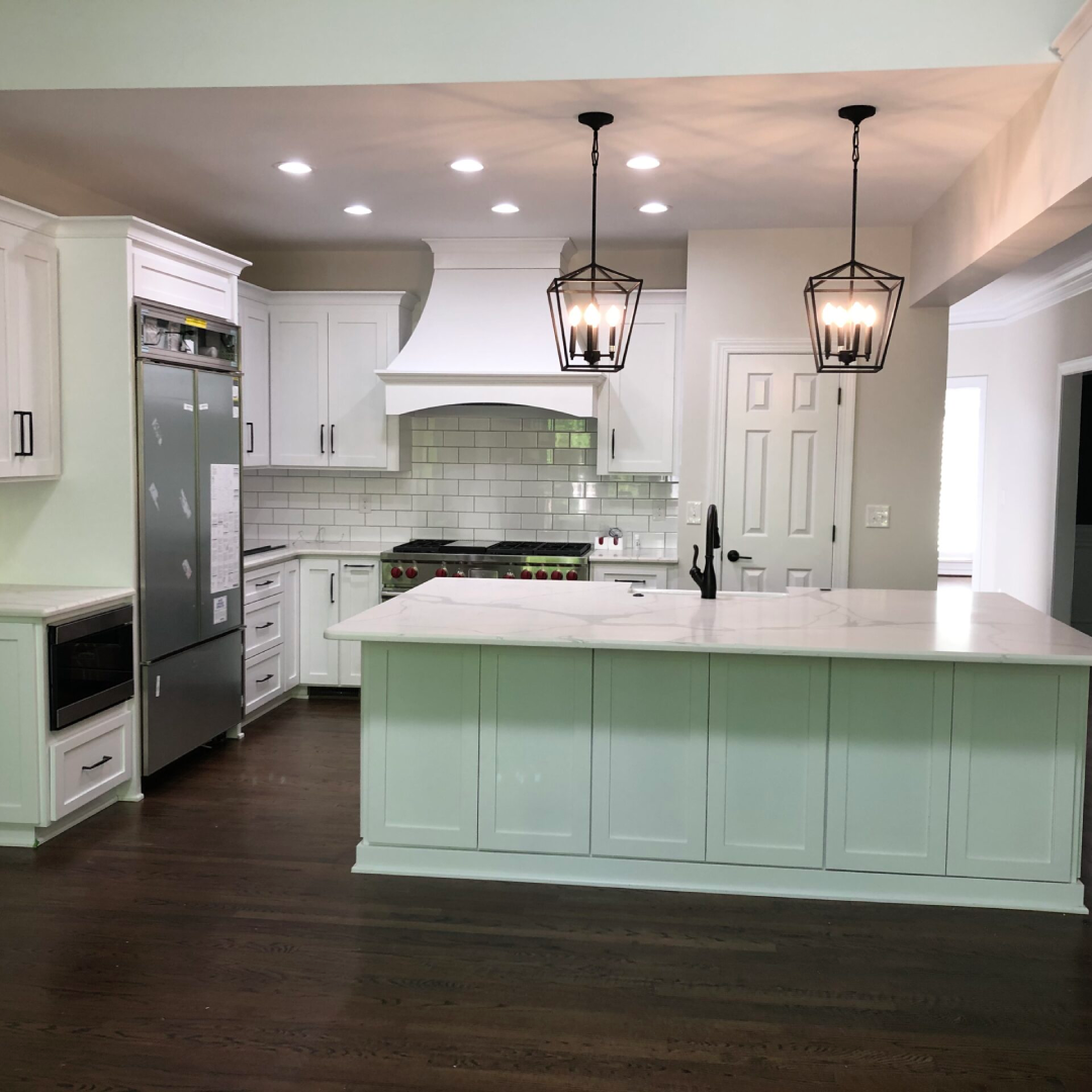 Modern kitchen with white cabinets, marble countertops, stainless steel appliances, subway tile backsplash, pendant lights, and hardwood floors.